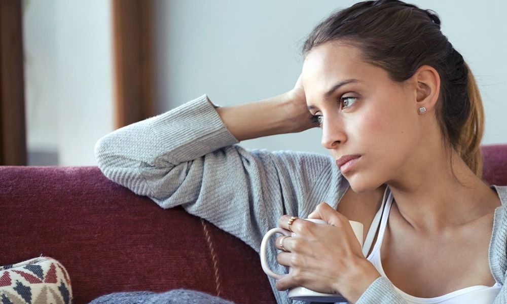 Junge Frau hält eine Tasse in der Hand und schaut nachdenklich.