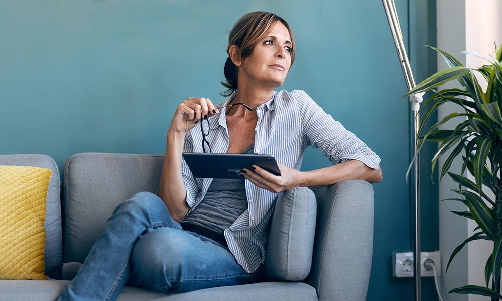 Frau sitzt auf dem Sofa und hält ein Tablet in der Hand.